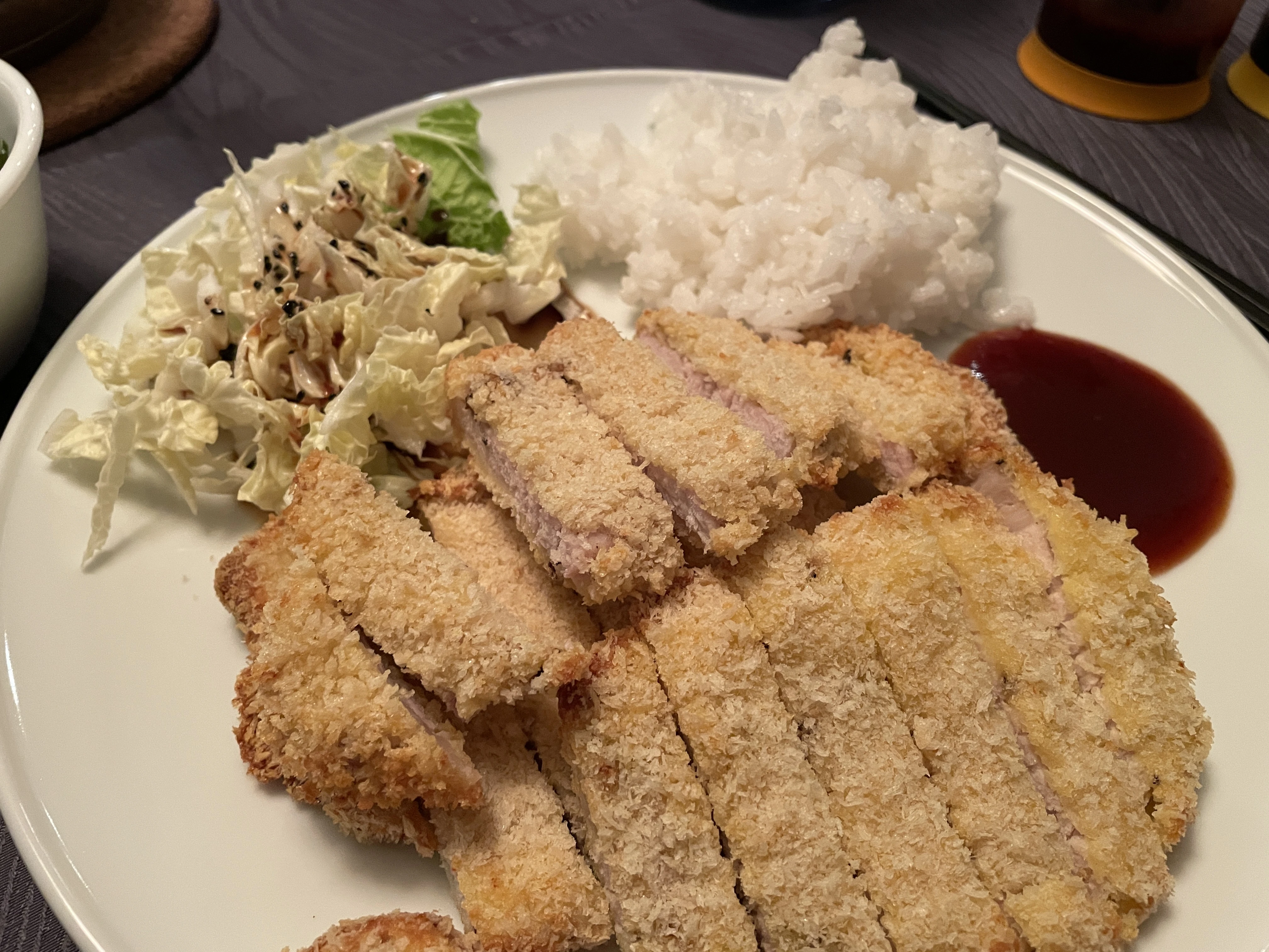 Three stacked sliced tonkatsu cutlets served with a salad and a scoop of rice.